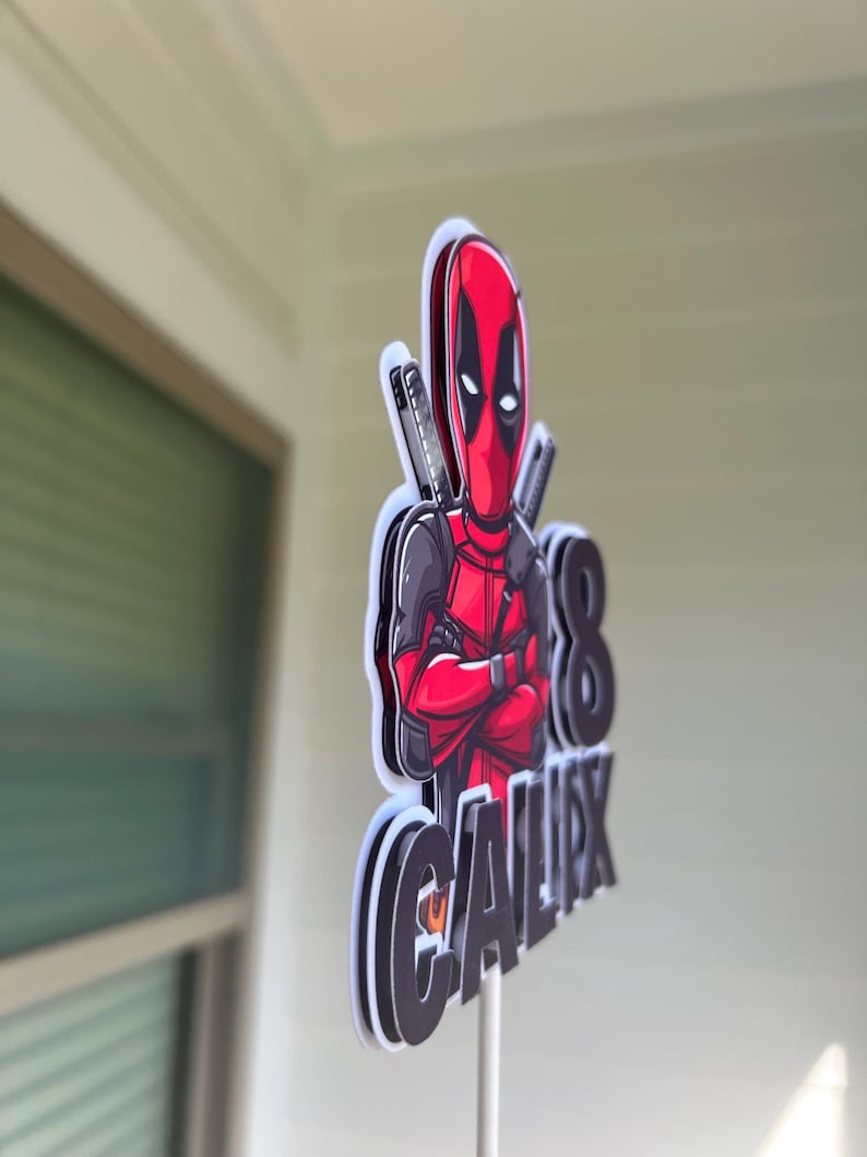 Op de afbeelding: Een rode en zwarte Deadpool-taarttopper met het nummer 8 en de naam "CALIX" erop.