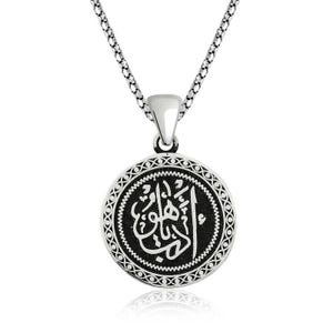 May include: A silver-colored pendant necklace featuring a circular pendant with Arabic calligraphy. The pendant has a black background with white text and a decorative border. The chain is a delicate, linked design.