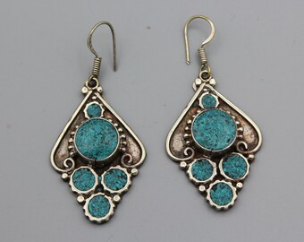 May include: A pair of silver dangle earrings with turquoise stones. The earrings have a teardrop shape and feature a large turquoise stone in the center, surrounded by smaller turquoise stones.