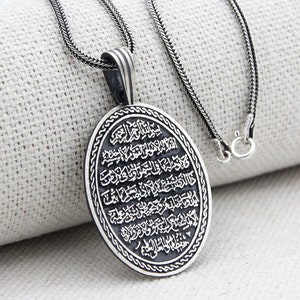 Op de afbeelding: Zilveren ketting met een ronde hanger met Arabische kalligrafie. De hanger is ovaalvormig en heeft een zilveren ketting.