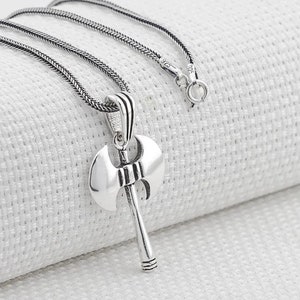 May include: Silver necklace with a double-headed axe pendant. The chain is a silver box chain.