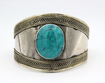 May include: A silver cuff bracelet with a turquoise stone set in the center. The bracelet has a decorative, braided design around the edges.