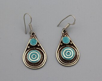 May include: A pair of silver dangle earrings with turquoise blue enamel detailing. The earrings feature a teardrop shape with a circular design in the center.