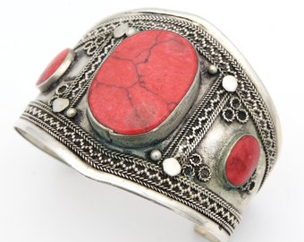 May include: Silver cuff bracelet with intricate detailing and three red oval stones.