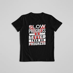 May include: Black t-shirt with a white graphic that says "Slow Progress is Better Than No Progress". The graphic is in a distressed font and has a red cross through the word "Slow".