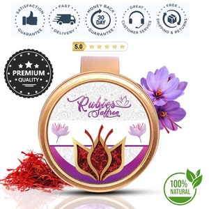 May include: A round, gold-colored container with a purple and white label that says "Rubies Saffron". The container is filled with red saffron threads. The image also shows a bunch of purple saffron flowers and a green leaf with the text "100% NATURAL".
