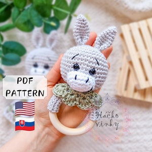 May include: Crocheted gray donkey rattle with green trim and a wooden ring. The rattle is handmade and features a US and Slovakian flag.
