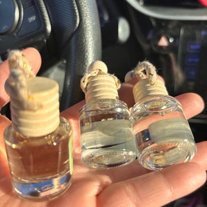 Op de afbeelding: Drie glazen flessen met houten doppen en touwtjes. De flessen zijn gevuld met een heldere vloeistof en worden in een hand gehouden.