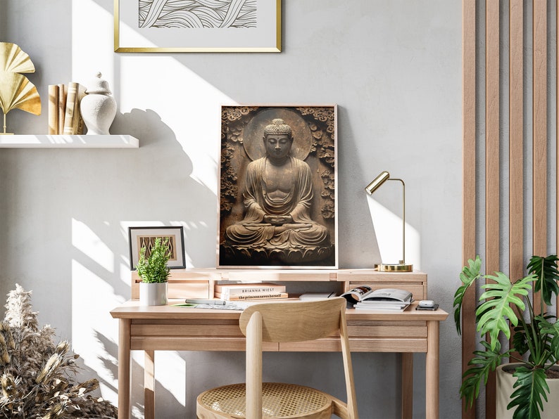 May include: A framed print of a brown stone Buddha statue sitting in meditation. The statue is surrounded by a carved floral design. The print is hanging on a white wall above a wooden desk with a chair.