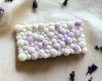Könnte beinhalten: Eine weiße Schokoladentafel mit einem violetten und weißen Marmormuster. Die Tafel ist rechteckig und hat eine leicht unregelmäßige Oberfläche.
