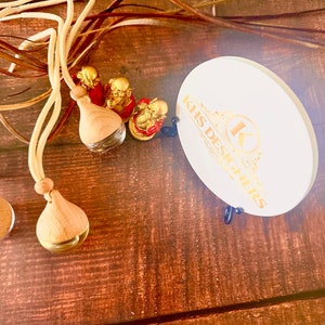 May include: Three wooden car air fresheners with gold accents and white string hanging from them. Three small gold figurines are in the background. A white round coaster with the text "KHS Designs" in gold lettering is in the upper right corner of the image.