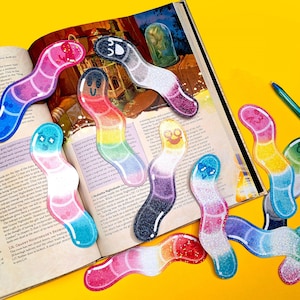 May include: A set of ten colorful glitter bookmarks shaped like gummy worms. Each bookmark has a different color and a different facial expression.