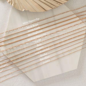 May include: A selection of rose gold necklaces in various styles, including Mini Paperclip, 3mm Rope, and Herringbone. The image displays the different chain designs on a white surface, with text labels identifying each style.