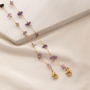 May include: Two delicate gold-colored chains with small, irregular purple gemstones and tiny gold beads. Each chain has a clasp at the end. The chains are likely for eyeglasses or a face mask.