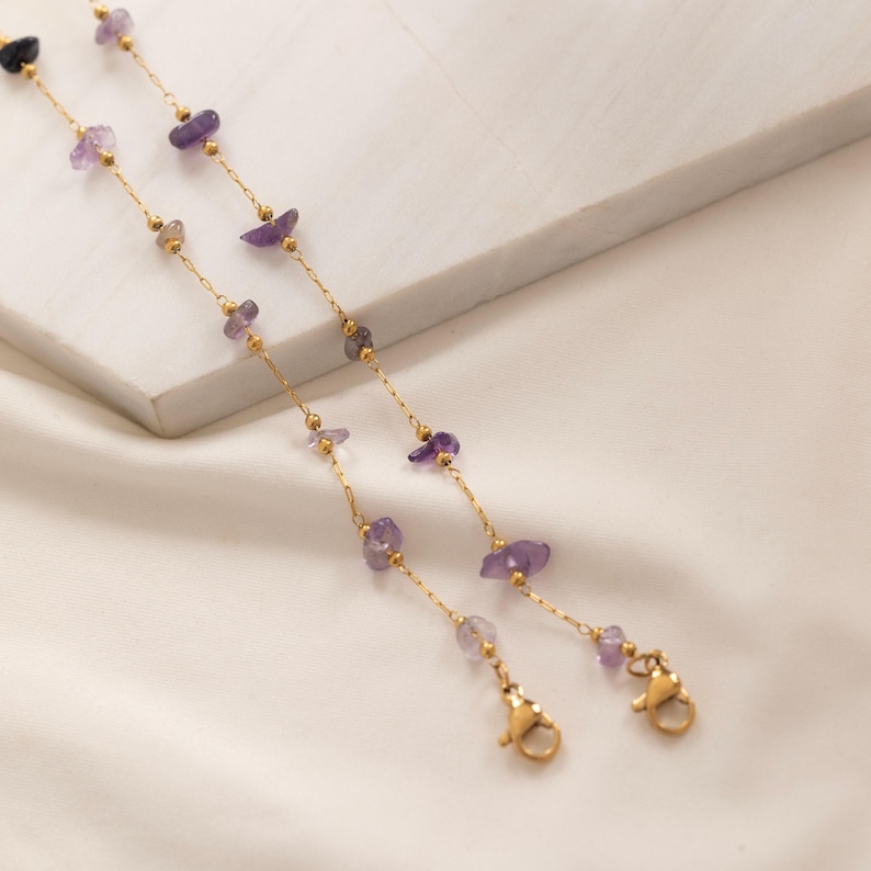 May include: Two delicate gold-colored chains with small, irregular purple gemstones and tiny gold beads. Each chain has a clasp at the end. The chains are likely for eyeglasses or a face mask.