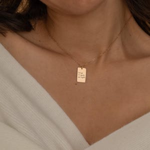 May include: A gold-colored rectangular pendant necklace. The pendant has the inscription "Love you to infinity and beyond" in a handwritten style. The necklace is worn around the neck.