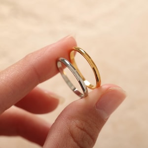 May include: Two thin rings, one gold and one silver, are held between fingers. The gold ring has a bright, shiny finish. The silver ring has a polished, reflective surface. Both rings are simple bands, likely for everyday wear.
