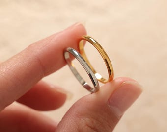 Può includere: Due anelli sottili, uno dorato e uno argentato, sono tenuti tra le dita. L'anello dorato ha una finitura brillante. L'anello argentato ha una superficie lucida e riflettente. Entrambi gli anelli sono semplici fasce, probabilmente per l'uso quotidiano.