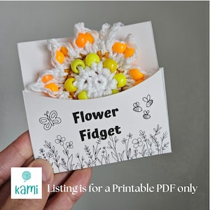 May include: A printable PDF pattern for a crocheted flower fidget toy. The flower is white with yellow and orange beads around the edges. The pattern is called "Flower Fidget" and is surrounded by a black and white illustration of flowers and bees.