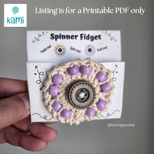 May include: A crochet spinner fidget toy featuring a beige yarn base with light purple beads and a dark brown center button. The item is attached to a white card with the text Spinner Fidget, Hold me, Spin me, Roll me, and Listing is for a Printable PDF only.