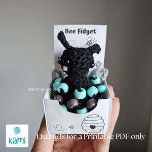 May include: A printable PDF pattern for crocheting a black bee with a blue and gray bead fidget toy. The pattern is called "Bee Fidget" and is available from @kamigoodies.