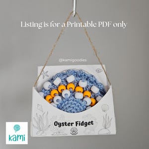 May include: A printable PDF pattern for an oyster-shaped crochet fidget toy. The toy is blue with white and yellow beads. The pattern is available for download.