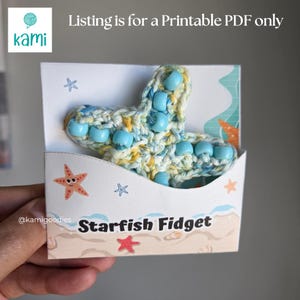 Peut inclure: Un jouet fidget en forme d'étoile de mer crocheté en fil bleu et jaune panaché, orné de perles en plastique bleu clair. L'objet est présenté dans une pochette en papier blanc illustrée d'étoiles de mer et du texte Starfish Fidget.