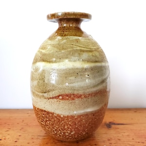 Könnte beinhalten: Eine Keramikvase mit brauner, weißer und gelber Glasur. Die Vase hat einen runden Körper und einen schmalen Hals.