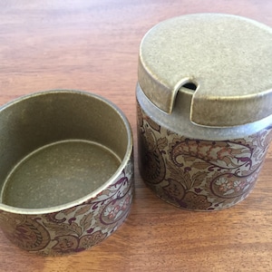 May include: A set of two ceramic containers with a paisley pattern in shades of green, brown, and purple. The containers have lids and are perfect for storing sugar or other kitchen staples.