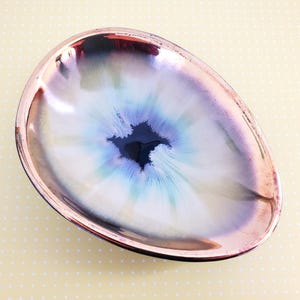 May include: An oval-shaped ceramic dish with a copper-colored rim. The inside of the dish is painted with a white, blue, and green swirl pattern with a black center.