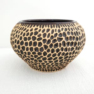 Pode incluir: Uma tigela de cerâmica marrom e bege com um padrão texturizado em forma de favo de mel.