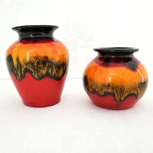 May include: Two ceramic vases with a red, orange and black glaze. The larger vase is taller and wider than the smaller vase.