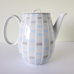 May include: A white ceramic teapot with a lid and a curved handle. The teapot is decorated with a grid pattern of light blue and grey rectangles on a white background. The spout is long and slender.