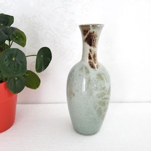 May include: A light green ceramic vase with brown and white speckled glaze. The vase has a narrow neck and a rounded body.