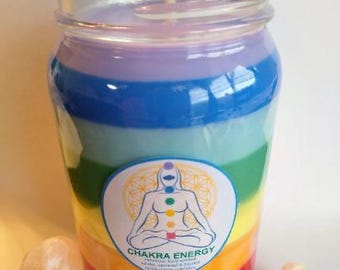 May include: A jar candle with a rainbow of colors, including red, orange, yellow, green, blue, and purple. The candle has a label with a human figure and the words "Chakra Energy." Several crystals surround the candle.