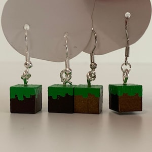 May include: Three pairs of silver dangle earrings with green and brown Minecraft block charms.