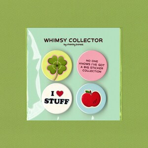 May include: A set of four whimsical pinback buttons in a clear plastic package. The buttons feature a four-leaf clover, the text "No one knows I've got a big sticker collection", "I love stuff", and a red apple.