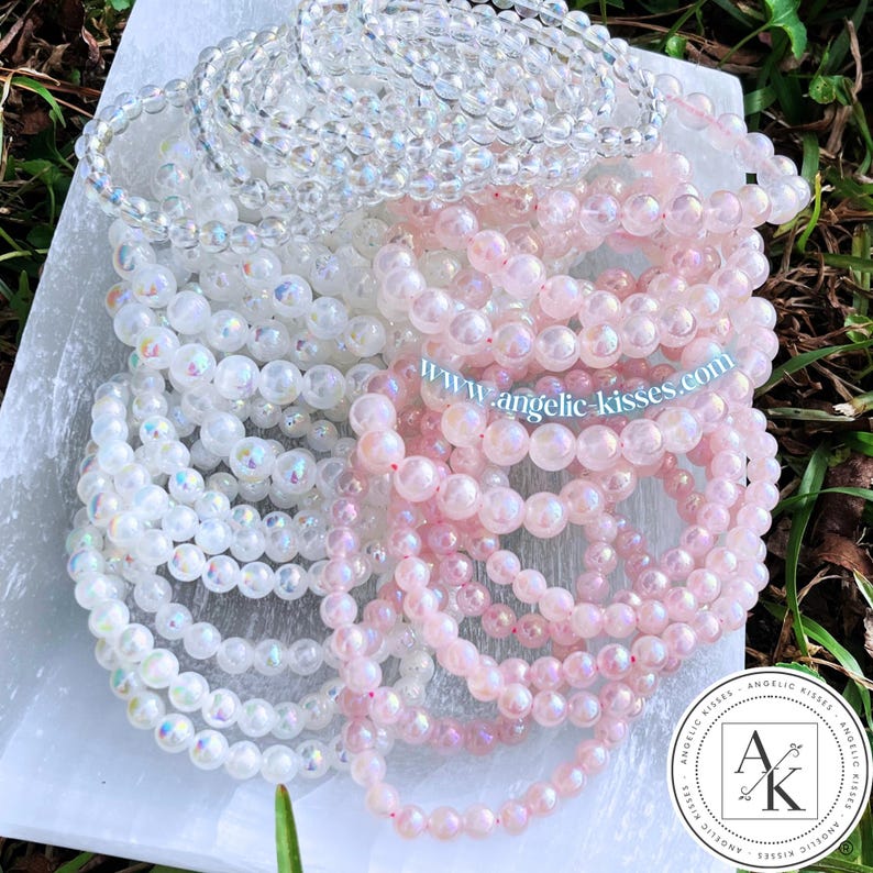Op de afbeelding: Een verzameling kralenarmbanden in heldere, witte en roze tinten. De armbanden zijn gemaakt van kleine, ronde kralen en zijn opgestapeld. Het websiteadres "www.angelic-kisses.com" is zichtbaar.
