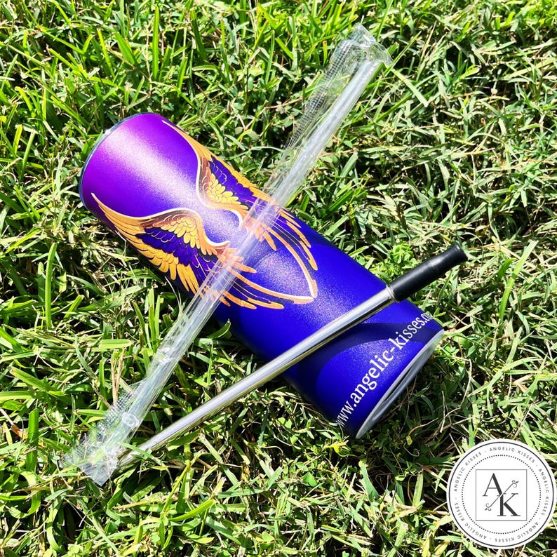 May include: A blue and purple tumbler with a gold wing design, a clear plastic straw, and a silver metal straw with a black tip. The tumbler has the website address www.angelic-kisses.com printed on it. The items are on a bed of green grass.