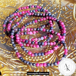 May include: Several beaded bracelets in shades of pink and dark blue are arranged on a gold-colored surface. The bracelets are made of small, round beads. The image includes a logo and the website address www.angelic-kisses.com.