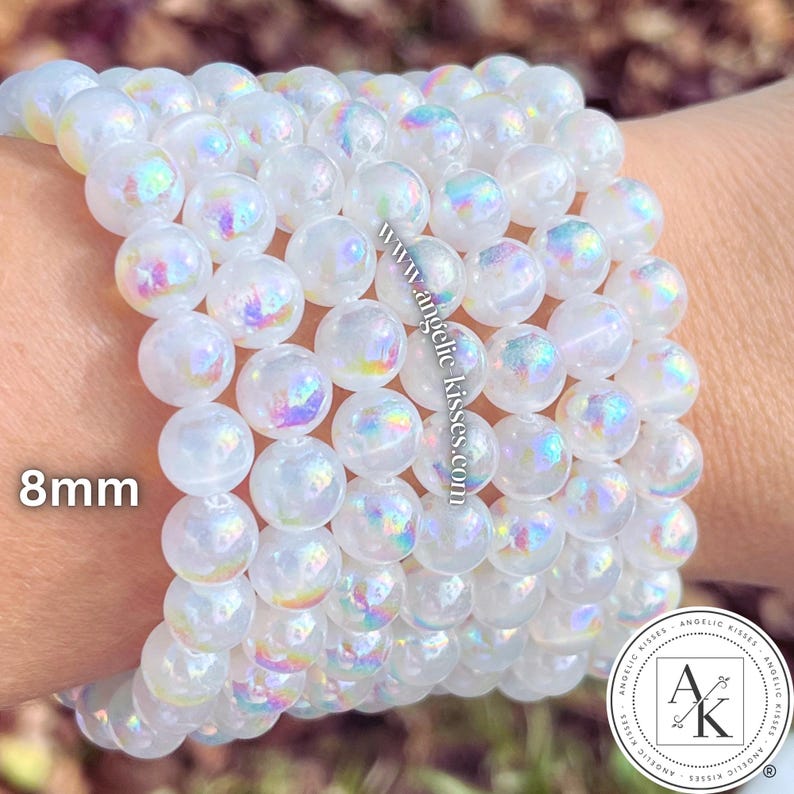 Op de afbeelding: Een stapel iriserende witte kralenarmbanden. De kralen hebben een diameter van 8 mm en hebben een glinsterend, regenboogachtig effect. De armbanden worden om een pols getoond.