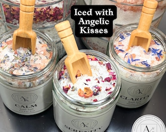 Pode incluir: Três frascos de vidro com sais de banho rotulados como Calm, Serenity e Clarity, cada um contendo uma pequena pá de madeira clara. Os frascos apresentam pétalas de flores secas e cristais de sal. O texto Iced with Angelic Kisses é visível.