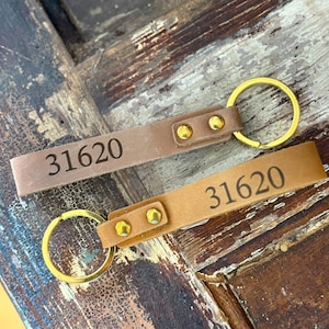 May include: Two leather keychains with gold-colored key rings. The keychains are brown and tan, each with the number "31620" printed on them. The leather straps are secured with gold-colored rivets.