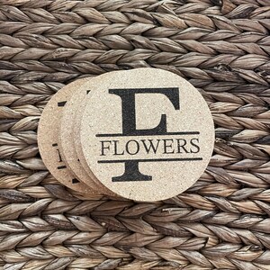 May include: Set of four cork coasters with a black and white design. The top coaster features the letter "F" and the word "FLOWERS" printed below the letter.