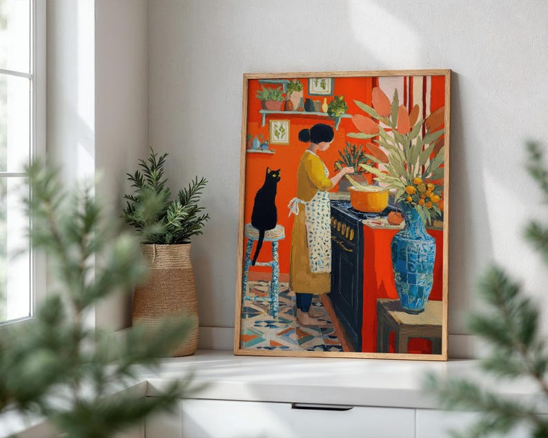 K&ouml;nnte beinhalten: Ein gerahmter Kunstdruck zeigt eine K&uuml;chenszene mit einer kochenden Person. Das Kunstwerk zeigt eine schwarze Katze, eine blaue Vase und einen leuchtend orangefarbenen Hintergrund. Die Person tr&auml;gt ein gelbes Kleid und eine Sch&uuml;rze.