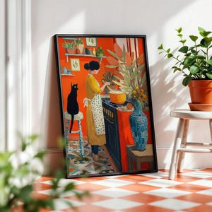 K&ouml;nnte beinhalten: Ein gerahmter Kunstdruck zeigt eine Frau in einem gelben Kleid, die in einer K&uuml;che mit einer orangefarbenen Wand kocht. Eine schwarze Katze sitzt auf einem Hocker. Eine blaue Vase und Topfpflanzen sind ebenfalls zu sehen.
