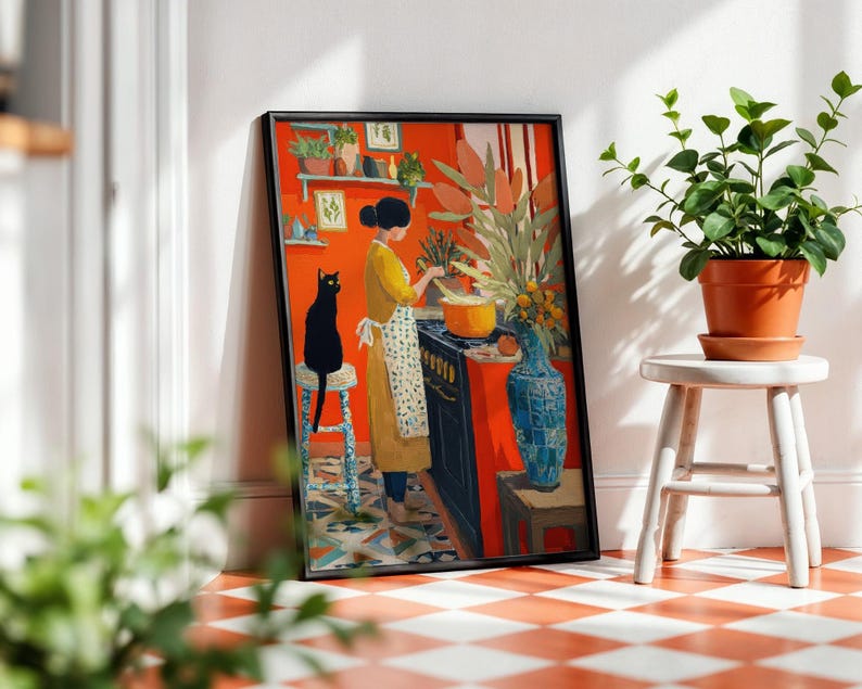 K&ouml;nnte beinhalten: Ein gerahmter Kunstdruck zeigt eine Frau in einem gelben Kleid, die in einer K&uuml;che mit einer orangefarbenen Wand kocht. Eine schwarze Katze sitzt auf einem Hocker. Eine blaue Vase und Topfpflanzen sind ebenfalls zu sehen.