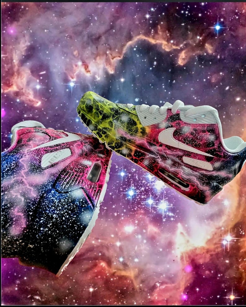 May include: A pair of white trainers with a galaxy-themed paint design. One shoe features a pink, blue, and white galaxy design, while the other shoe has a green, yellow, and black galaxy design.