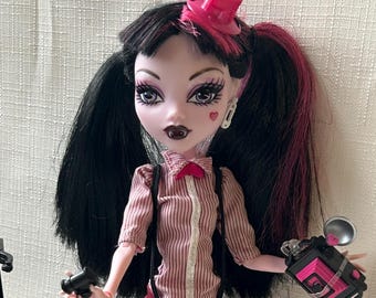 Pre-owned Monster High Doll – Draculaura Newspaper Club edition. Authentic Mattel collectible. Includes doll and stand.