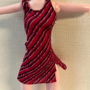 Puede incluir: Vestido de mu&ntilde;eca a rayas rojas y negras, con cuello halter y abertura lateral. El vestido sin mangas es de tejido. Las rayas diagonales crean un patr&oacute;n din&aacute;mico. Vestido para mu&ntilde;eca.
